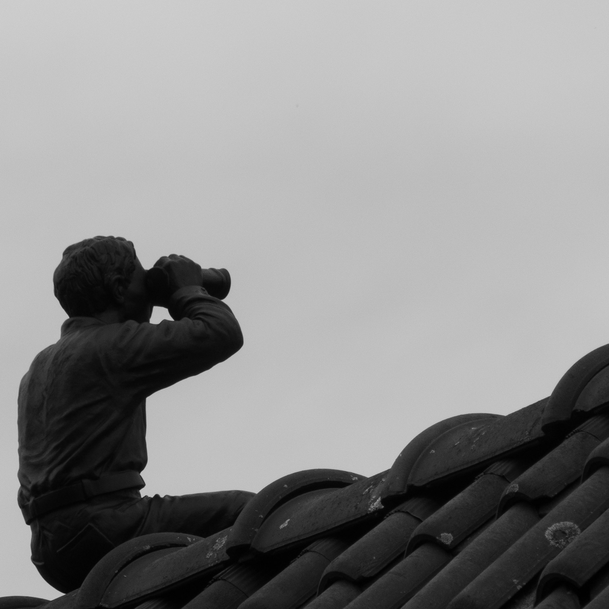 Standbeeld van verrekijkend mannetje op dak