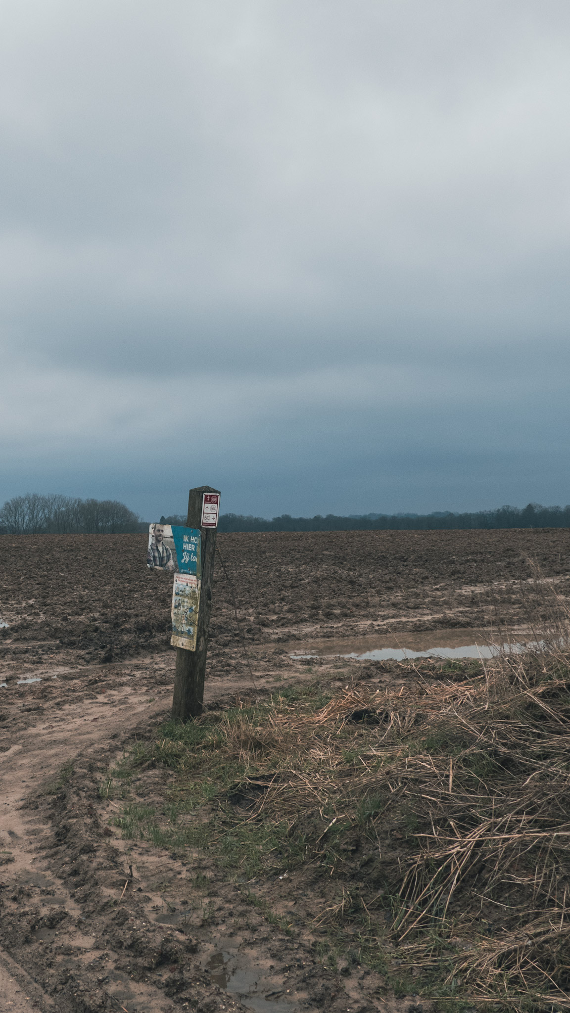 Een wandelknooppuntpaaltje dat je een zeer modderige weg opstuurt